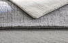 Close-up of three overlapping rectangular rugs in neutral tones, showcasing different shades of gray and beige as well as contrasting soft and textured surfaces.
