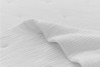 A close-up of a white, textured fabric sheet gently draped over a mattress, creating soft folds and a clean, minimalist appearance.