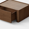 A minimalist wooden rectangular box with a single drawer partially open, placed on a light gray surface against a plain white background.