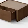 A minimalist wooden rectangular box with a single drawer partially open, placed on a light gray surface against a plain white background.