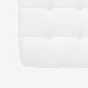 Close-up of the corner of a white mattress, showing tufted stitching and a textured fabric surface with piped edges.