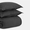 A neatly folded dark gray duvet with two matching pillows stacked on top, all set against a plain white background.