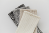 Four pairs of knitted socks in neutral colors—black, gray, beige, and off-white—are arranged in an overlapping fan shape on a white background.