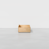 A simple wooden storage box with short sides and an open top sits on a smooth, light gray floor against a plain white background.