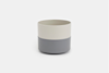A cylindrical cup with a two-tone design, featuring a light beige upper half and a gray lower half, placed on a plain white background.