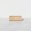 A rectangular, light wood storage box with an open top, placed on a smooth grey floor against a plain white background.