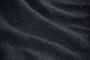 Close-up of a dark, textured fabric with visible weave and gentle horizontal folds, creating a patterned and slightly wavy surface.