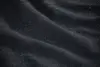 Close-up of a dark, textured fabric with visible weave and gentle horizontal folds, creating a patterned and slightly wavy surface.