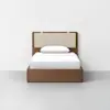 A single bed with a wooden frame, a light beige upholstered headboard, and white bedding, positioned against a plain white wall on a light gray floor.