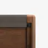 Close-up of the corner of a wooden furniture piece with a soft, gray fabric cover on top and rounded edges, showing a blend of wood and fabric materials against a white background.