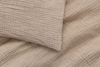 A close-up view of a beige, textured bedding set featuring a pillow and a blanket with a crinkled, grid-like quilted pattern.