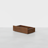 A rectangular, open wooden box with smooth, dark brown finish sits on a light gray surface against a plain white background.