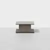 A rectangular, modern coffee table with a thick central pedestal base and a sleek, minimalist design in a light gray wood finish, set against a plain white background.