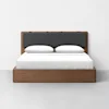 A modern wooden bed with a simple frame, a dark upholstered headboard, white sheets, and two white pillows, set against a plain white wall and grey floor.