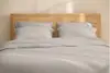 A neatly folded stack of white bed linens, including sheets and pillowcases, set against a plain white background.