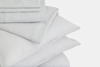 A neatly folded stack of white bed linens, including sheets and pillowcases, set against a plain white background.