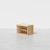 A small, light wood storage unit with two open shelves, placed on a plain light gray floor against a white background.