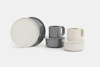 Two sets of modern dishware, each with a plate, bowl, and mug, in neutral tones of gray and cream, arranged on a white background.
