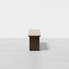 A minimalist wooden table with a rectangular top and solid base, photographed against a plain white background. The table casts a subtle shadow on the light-colored floor.