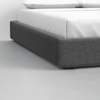 Close-up view of the lower corner of a bed with a dark gray upholstered frame and white bedding, set on a light gray floor.