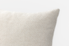 Close-up of the top right corner of a textured, off-white fabric pillow against a plain white background.