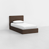 A single bed with a dark wooden frame, white sheets, and a white pillow, set against a plain white wall and light gray floor.
