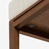 Close-up view of a wooden table or bench corner with a light-colored cushioned seat and a small round button or port underneath the surface.