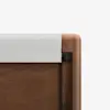 Close-up of the top corner of a wooden crib with a white fabric rail cover, showing smooth wood grain and rounded edges against a plain white background.