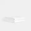 A neatly folded, white towel stacked on a plain white surface with a light gray background.