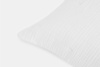 Close-up of the corner of a white pillow with a textured, wavy pattern on the fabric, set against a plain white background.