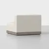 A modern armless corner sofa with light beige upholstery and a wooden base, displayed in a minimalistic, light gray setting.
