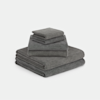 A neatly stacked set of dark gray towels in various sizes, arranged in a pyramid shape on a plain white background.