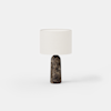 A modern table lamp with a cylindrical white fabric lampshade and a dark, marbled stone base, set against a plain white background.