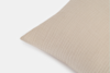 A close-up of a beige, textured fabric pillow with a subtle grid pattern, shown against a plain white background.