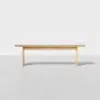 A simple, light wood bench with clean lines, positioned on a smooth, light gray floor against a plain white background.