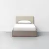 A minimalist single bed with a light beige upholstered headboard, white bedding, and a wooden base, set against a plain white wall and gray floor.