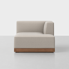 A modern, light beige upholstered sectional sofa with a low wooden base and right-side armrest, set on a smooth light gray floor against a plain white background.