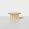 A minimalist, round wooden table with a thick top and a solid rectangular base, set against a plain white background.