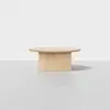 A minimalist, round wooden table with a thick top and a solid rectangular base, set against a plain white background.