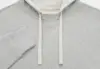 Close-up of a light gray hoodie with a V-shaped stitching below the collar, cream-colored drawstrings, and a ribbed cuff on the left sleeve. The fabric appears soft and textured.