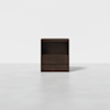 A modern, dark brown wooden nightstand with an open shelf above two closed drawers, placed on a plain, light gray floor against a white background.