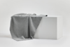 A light gray knit blanket is draped over a large white rectangular block against a plain white background.