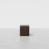 A dark brown, wooden rectangular box or pedestal sits alone on a smooth, light gray surface with a plain white background.