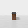 A minimalist wooden bench with a black cushioned seat, photographed against a plain white background. The bench is centered and viewed from the front.