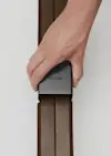 A hand is connecting two dark wooden beams using a black metal joint piece labeled THUMA against a plain white background.