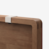 A close-up of the corner of a wooden tabletop with rounded edges, featuring a light-colored fabric strap fastened around the top edge. The background is plain white.