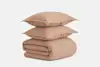 A folded beige comforter with two matching beige pillows stacked neatly on top, set against a plain white background.