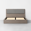 A modern wooden bed frame with a light gray upholstered headboard, shown without a mattress, against a plain white wall and gray floor.