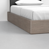 A close-up view of a modern bed with a light wood platform base and white bedding, set on a smooth light gray floor.