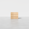 A minimalist wooden dresser with three drawers stands on a smooth, light gray floor against a plain white background.